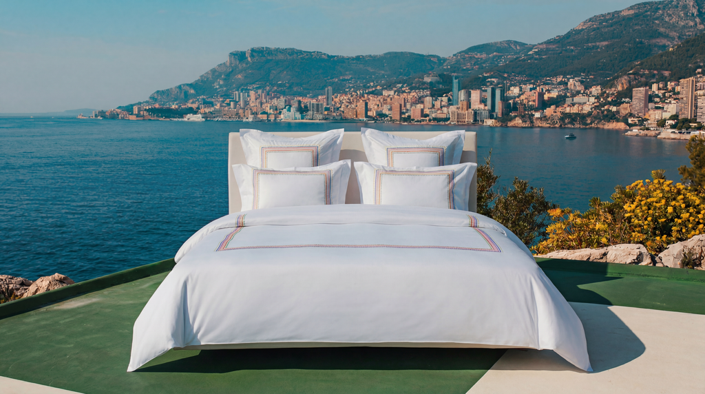 White bed with a scenic view of a coastal city and mountains.