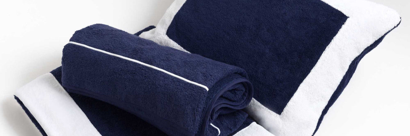 A set of folded bath towels in navy and white colors with embroidered detailing on the white towels.