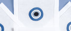 A set of white hand embroidered drink placemats with a blue Greek eye design on a blue background, displayed folded.
