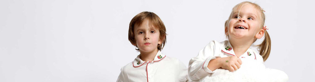Three children in matching white outfits with red accents on a plain background