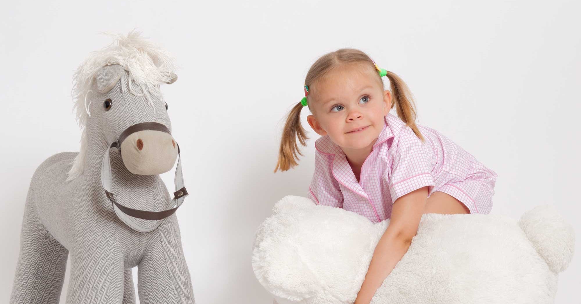 Child playing with a stuffed horse and a large white teddy bear on a white background