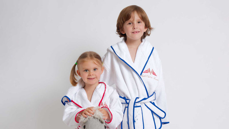 Two children wearing white martial arts robes with red and blue accents on a light gray background