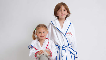 Two children wearing white martial arts robes with red and blue accents on a light gray background
