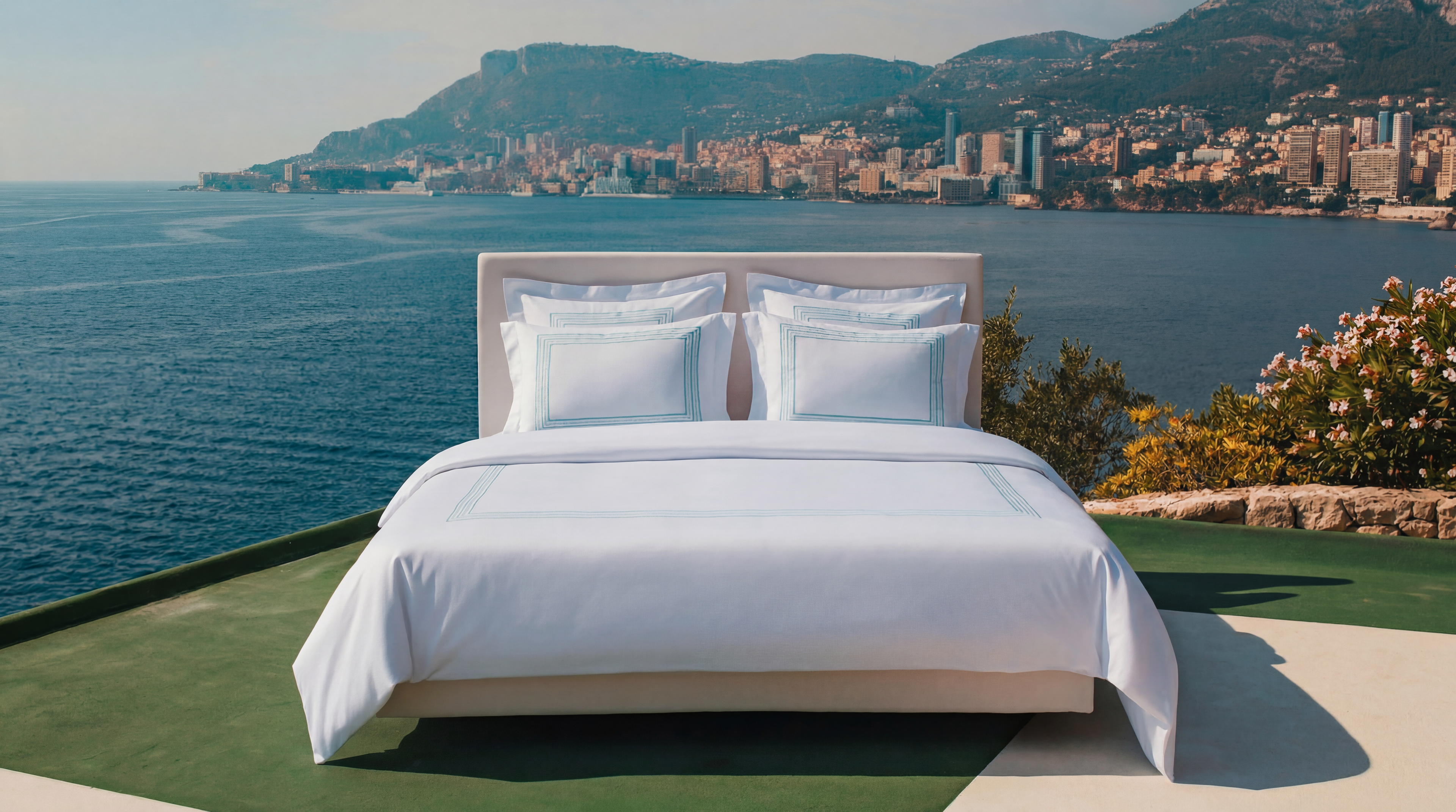 Bed with white bedding overlooking a scenic coastal view with mountains and buildings.
