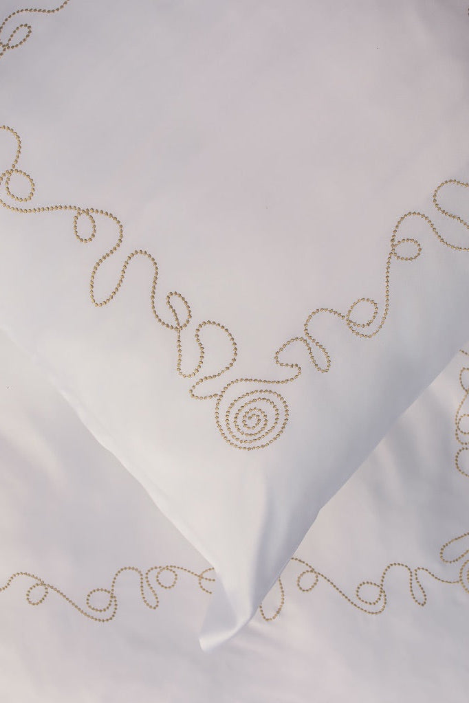 Maison Alia luxury bedding - gold spiral hand-embroidery detail on premium white linen, artisan craftsmanship