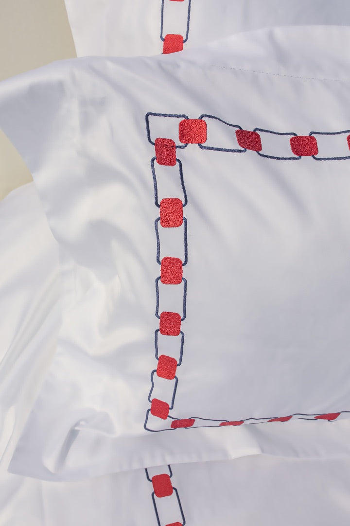 Maison Alia luxury bedding - closeup of red and blue hand-embroidery detail on premium white linen, artisan craftsmanship