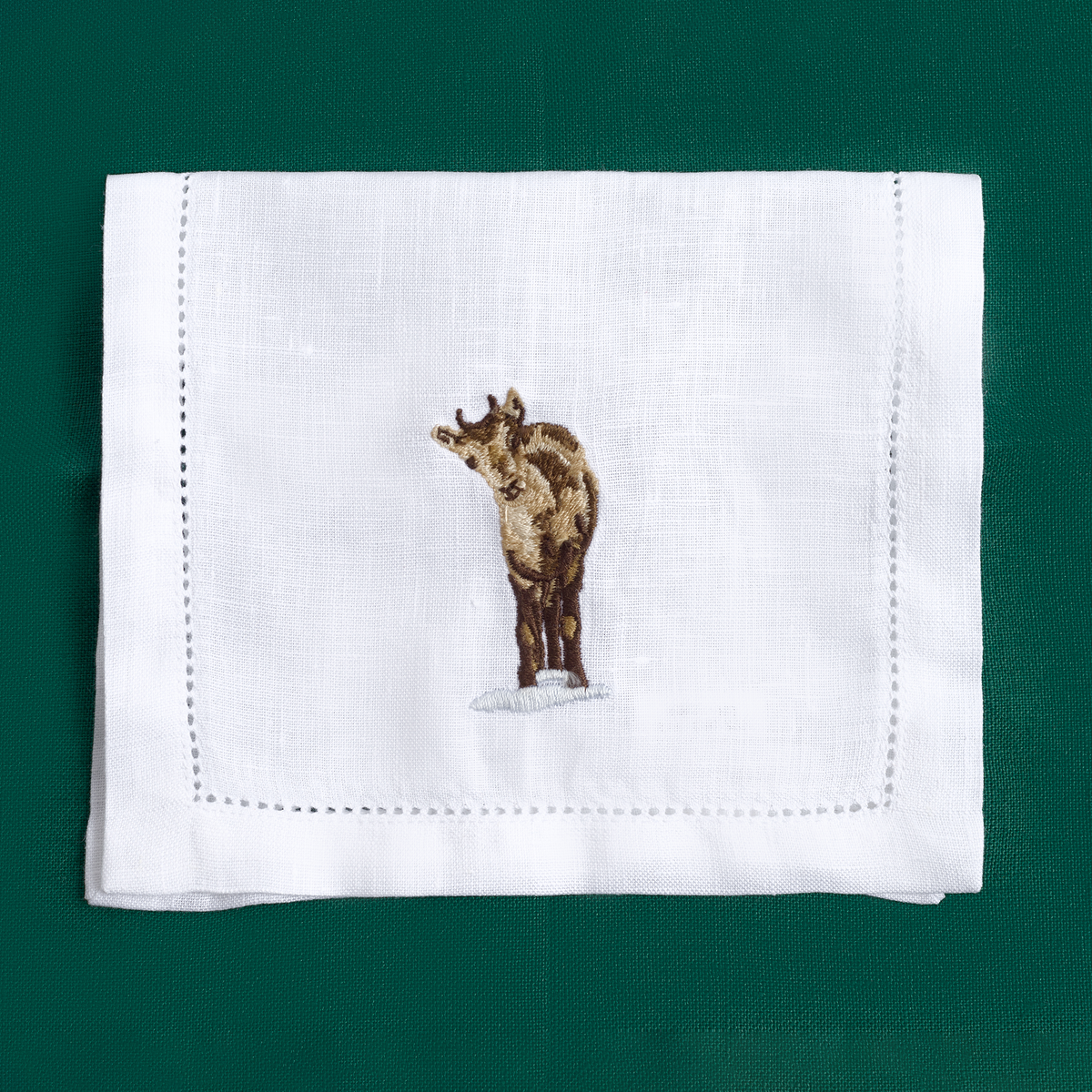 Close-up of embroidered alpine animal on white linen cocktail napkin