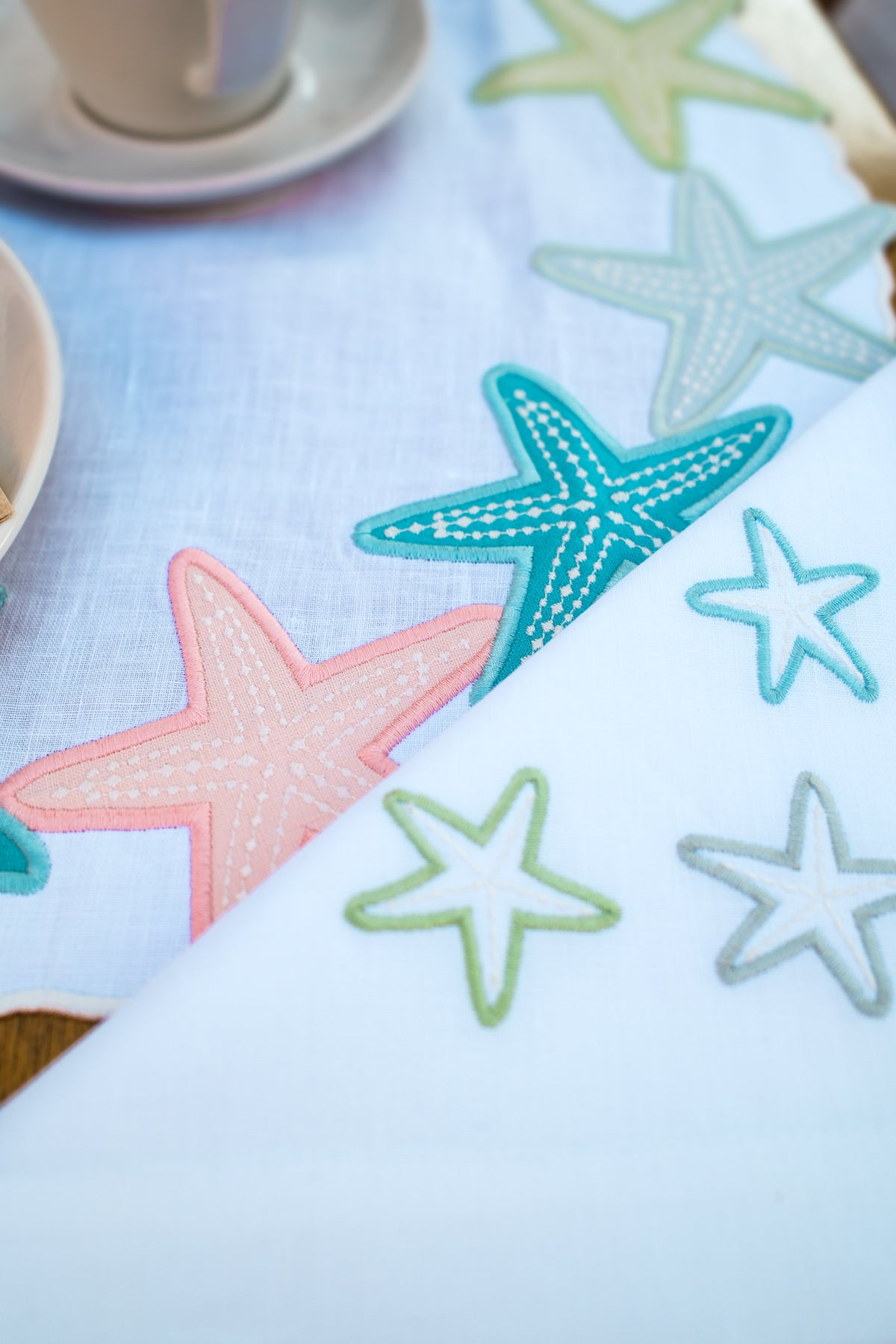 Close-up of pastel embroidered starfish on scalloped white linen placemat